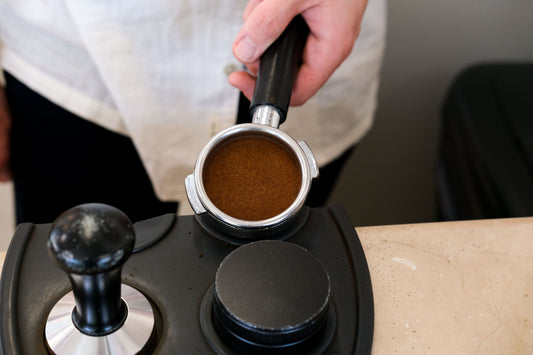 Barista holding a prepared espresso portafilter beside a tamper before extraction