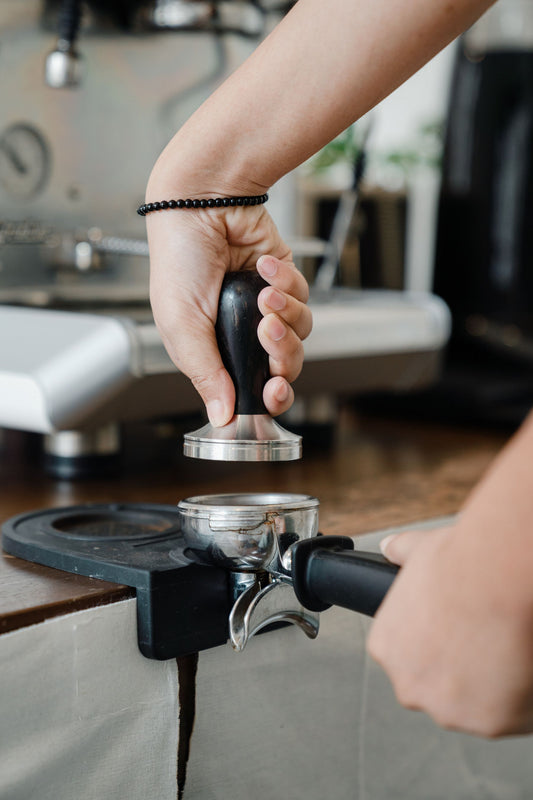 Barista tamping ground coffee in an espresso portafilter during puck preparation